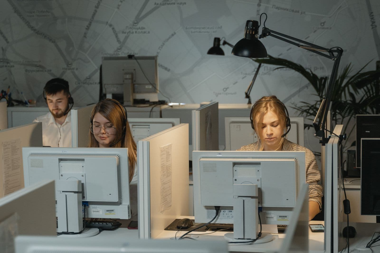 Tres agentes de un centro de atención al cliente con auriculares trabajan frente a sus ordenadores en cubículos de oficina.