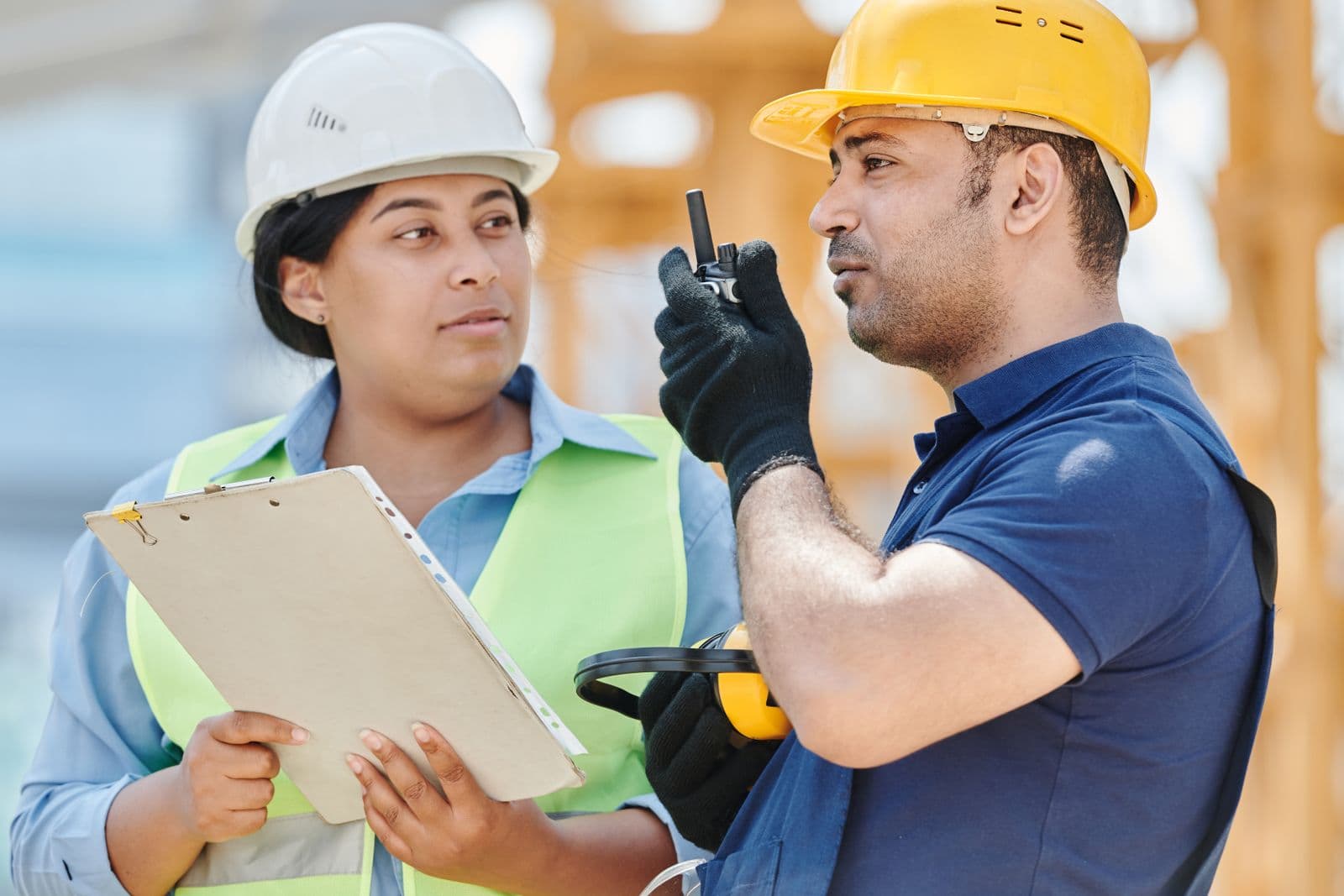 Dos operarios de obra con casco y chaleco reflectante se comunican por radio en un solar en construcción.